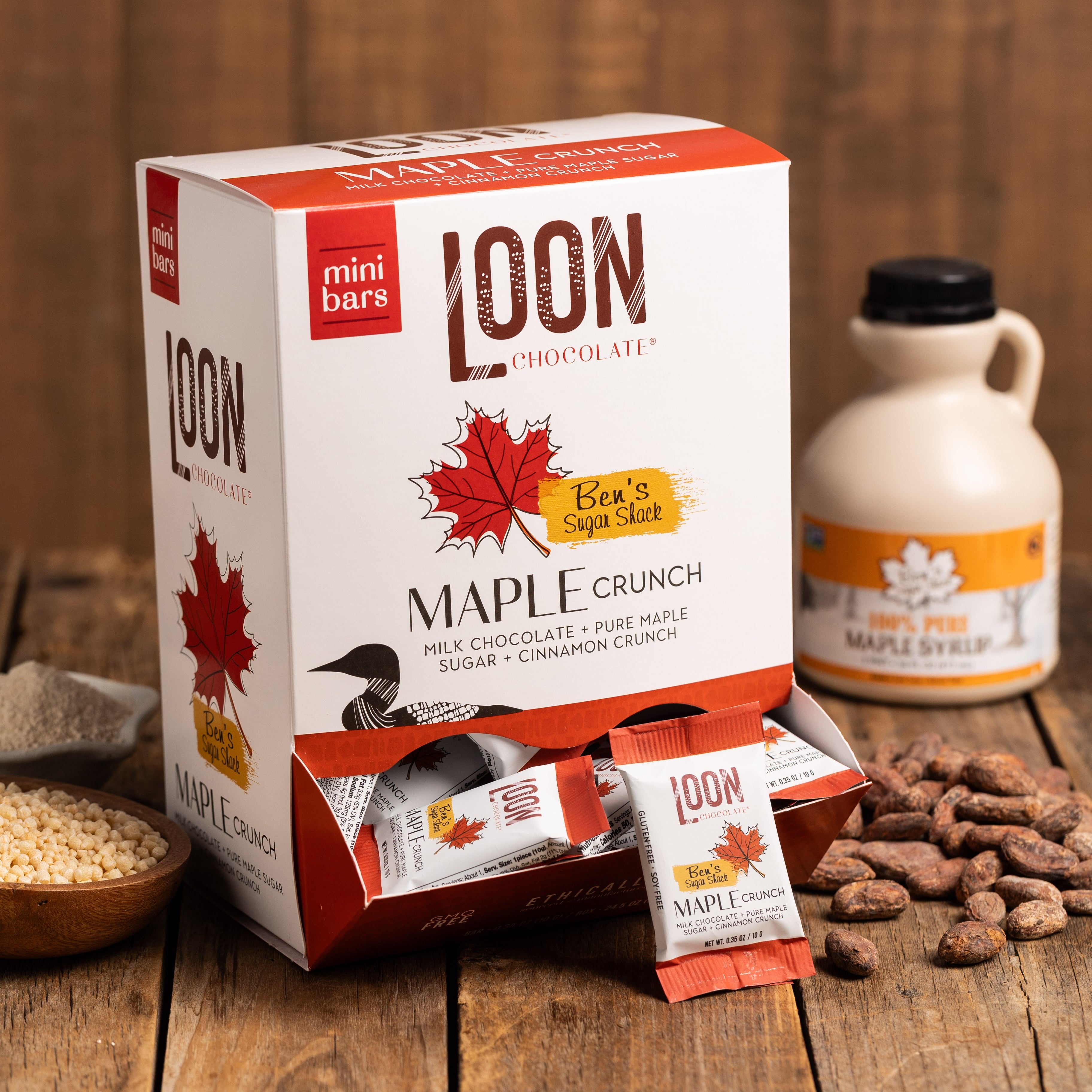 Box of Maple Crunch Milk Chocolate mini bars by Loon Chocolate on wooden surface with cacao beans