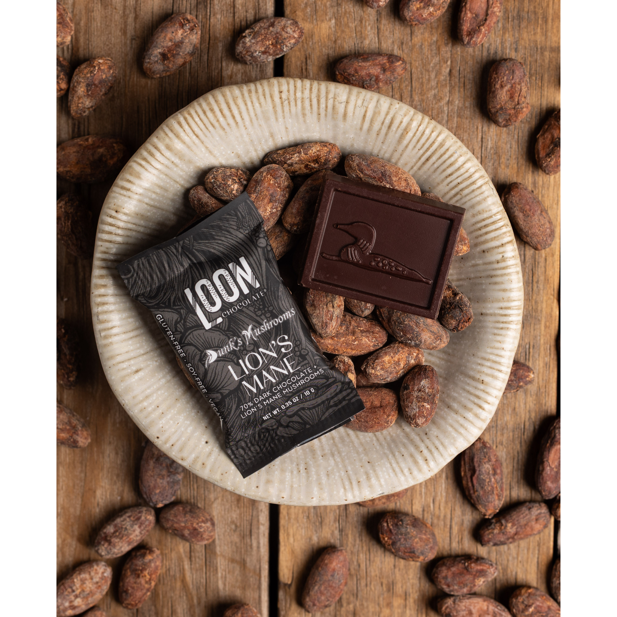 Lion's Mane Dark Chocolate Mini Bar by Loon Chocolate on wooden surface with cacao beans
